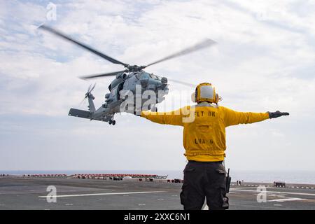 240821-N-TW227-1028 STRETTO DI MIYAKO (21 agosto 2024) Un marinaio assegnato alla nave d'assalto anfibia schierata in avanti USS America (LHA 6), segnala un MH Foto Stock