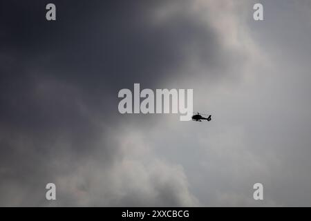 Un elicottero che vola contro un cielo spettacolare pieno di nuvole scure. L'immagine cattura il contrasto tra l'aereo e l'atmosfera soffusa. Foto Stock