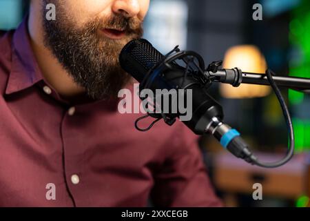 Primo piano di un artista ASMR che utilizza un microfono di qualità in studio per realizzare video anti-stress, sussurrando suoni formicolosi. Uomo che usa un microfono professionale per dormire e che induce un audio di alta qualità per la meditazione Foto Stock