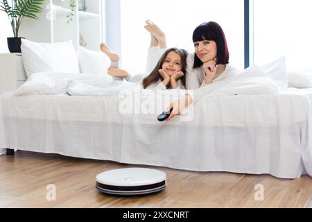 Mamma e figlia si rilassano sul letto con l'aspirapolvere robotizzato Foto Stock