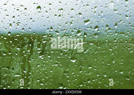 Lo sfondo naturale cade su entrambi i lati del vetro dalla pioggia e dalla visuale astratta appannante, le gocce di pioggia sul vetro blu e la sfocatura Foto Stock