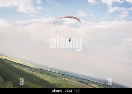 Un parapendio bianco-arancio vola sul terreno montuoso Foto Stock