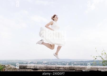 La sposa pazza salta e si aggrappa nel cielo sullo sfondo del paesaggio urbano di una piccola località turistica nel Caucaso settentrionale. Il concetto di divertimento A. Foto Stock