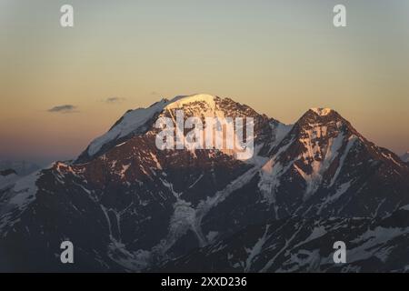 Un panorama al tramonto dell'elbrus e parte della cresta caucasica con nuvole arancioni e un ghiacciaio incrinato sul fondo Foto Stock