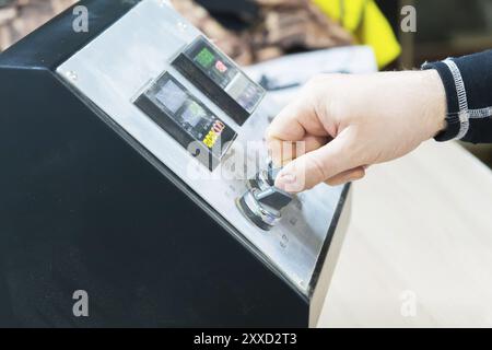 Un primo piano della mano di un uomo tiene un interruttore rotativo sul pannello di controllo dell'attrezzatura con gli strumenti Foto Stock