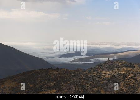 Escursionista il vincitore si trova sul bordo della roccia con bastoncini sollevati di fronte alla valle coperta da nuvole nel Caucaso. Il concetto di motivazione Foto Stock