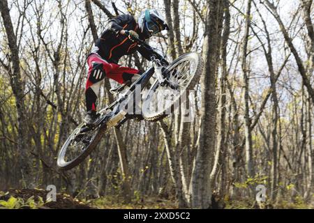 Un giovane pilota al volante della sua mountain bike fa un trucco nel saltare sul trampolino di lancio del sentiero di discesa nella foresta autunnale. Il co Foto Stock