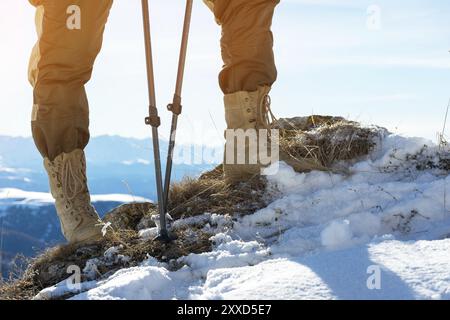 Primo piano del piede di un turista con stivali da trekking con bastoni per il nordic walking in piedi su una pietra nelle montagne caucasiche Foto Stock