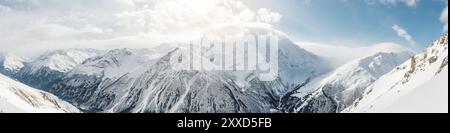 Panorama della cresta caucasica con nuvole appese sulle cime delle montagne coperte di neve fotografate dal pendio del vulcano Elbrus Foto Stock