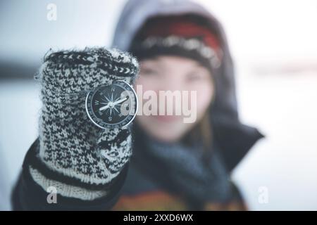 La giovane donna sorridente regge una bussola. Inverno, guanti e cappuccio Foto Stock