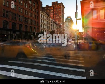 Taxi gialli che attraversano un trafficato incrocio sulla 23rd Street a New York City con effetto di sfocatura del movimento e sfondo alla luce del sole Foto Stock