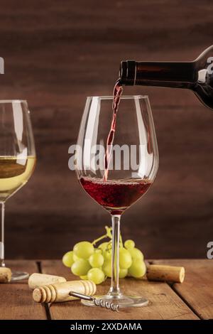 Vino rosso che viene versato in un bicchiere da un flacone, su uno sfondo scuro, con un posto per il testo e per le uve nel sfondo sfocato. Modello di progetto fo Foto Stock