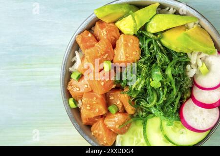 Invio di un poke di salmone con avocado, wakame e cetrioli, overhead close-up shot su un teal sfondo blu con spazio di copia Foto Stock