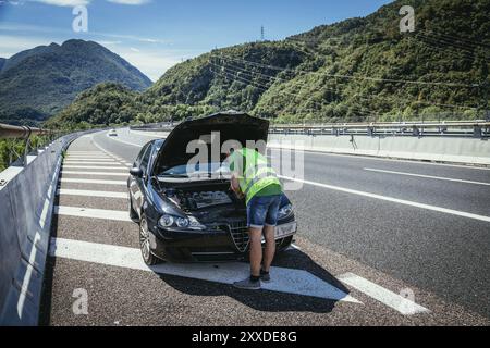 Meccanico in giubbotto riflettente sta cercando di riparare un guasto auto sulla strada, cofano motore Foto Stock