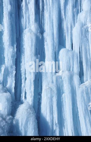 Grandi ghiaccioli pendono dalla scogliera della riva del fiume. Sfondo blu Foto Stock