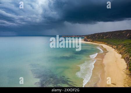 Vista aerea della pioggia che cade dalle nuvole di tempesta scure che si innalzano su una tranquilla spiaggia costiera di Torquay sulla Great Ocean Road a Victoria, Australia. Foto Stock