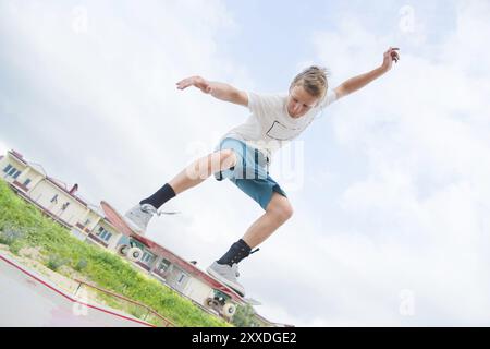 Giovane e intenso skateboarder in salto in alto contro il cielo e le zone notte Foto Stock