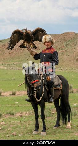 Issyk Kul, Kirghizistan - 23 maggio 2022: Addestratore di aquile a cavallo con la sua aquila d'oro, che mostra le tradizionali tecniche di caccia tramandate fino alla g Foto Stock