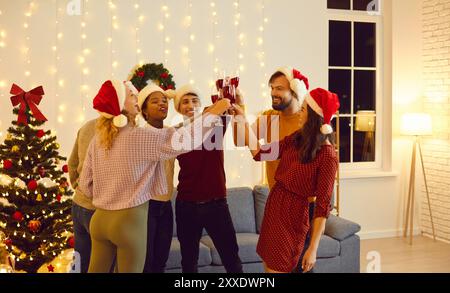 Gli amici festeggiano le vacanze invernali a casa e brulicano bicchieri di vino augurando buona fortuna e gioia. Foto Stock