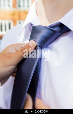 Una persona sta sapientemente legando una cravatta blu intorno al collo di una camicia mans in modo meticoloso, mostrando la sua attenzione ai dettagli Foto Stock