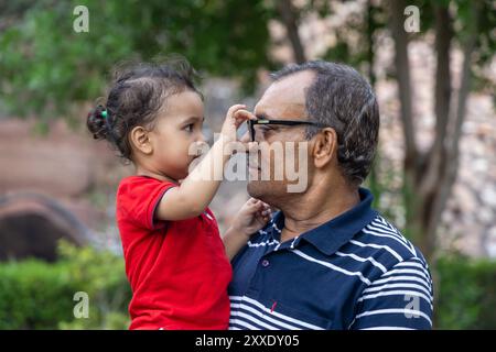 Nipote che gioca con gli occhiali del nonno al Dusk in Park Foto Stock