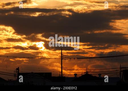 Un tramonto in un cielo nuvoloso sopra case e pali del telegrafo a Kanagawa, Giappone. Foto Stock