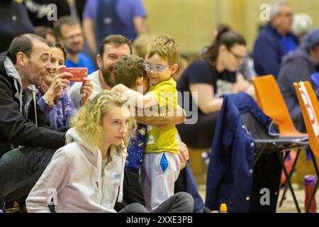 A un roller derby in un palazzetto dello sport di Loughborough, due piccoli ragazzi si abbracciano in modo affascinante al piacere dei due uomini e di una donna con loro Foto Stock