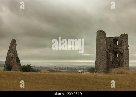 Castello di Hadleigh, Regno Unito. 24 agosto 2024. Rovine di una storica struttura in pietra su una collina erbosa, caratterizzata da un'alta parete a punta e da una torre parzialmente intatta con aperture delle finestre. La scena si affaccia su una città lontana e su un corpo d'acqua sotto un cielo nuvoloso, evocando temi del patrimonio, dell'isolamento e del degrado atmosferico. Un inizio bagnato e cupo per il fine settimana festivo al Castello di Hadleigh, affacciato sull'estuario del Tamigi. Penelope Barritt/Alamy Live News Foto Stock