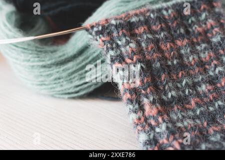 Palla colorata in filato con calzino a maglia e aghi per maglieria. Fili in alpaca e lana con un bel motivo a maglia. Woolen uncinetto da vicino. Foto Stock