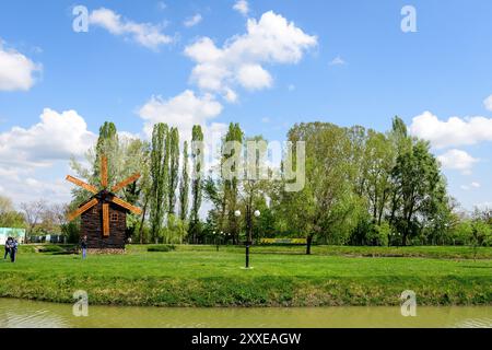 Piccolo lago con un mulino a legna e un'isola dal Parco Chindiei (Parcul Chindiei) a Targoviste, Romania, in una soleggiata giornata primaverile con nuvole bianche e blu Foto Stock