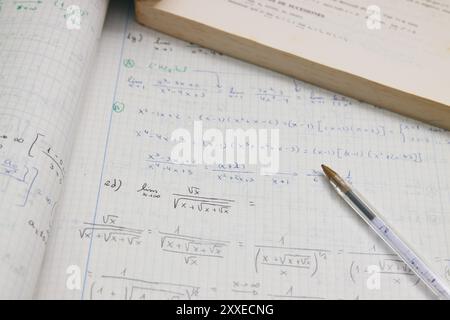 Immagine di un notebook con esercitazioni matematiche avanzate (limiti) accanto a una penna e al libro dello studente Foto Stock