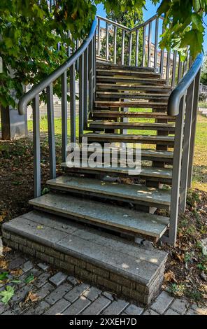 Angolo di curva della scala pubblica in cemento con corrimano in metallo, incorniciato da foglie verdi in un parco cittadino. Foto Stock