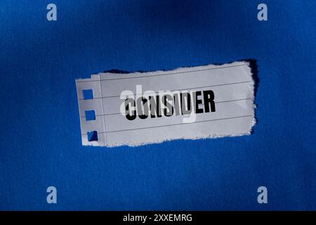 Considerare il messaggio scritto su un pezzo di carta strappato con sfondo blu. Simbolo concettuale da considerare. Copia spazio. Foto Stock