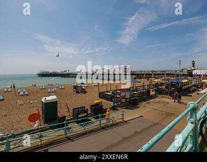 Una vista panoramica del Brighton Pier England presa dal lato sinistro del molo che mostra la spiaggia e il caffè in primo piano con rampa di accesso alla spiaggia. Foto Stock