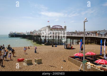 Vista panoramica del molo di Brighton in Inghilterra con spiaggia in primo piano e gente che si gode la giornata di sole. Foto Stock