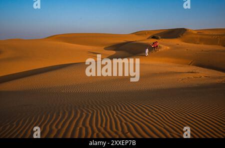 Una serena scena di ampie dune di sabbia al tramonto con un viaggiatore solitario che conduce un cammello, catturando la bellezza tranquilla di un paesaggio desertico a Jaisalmer , Foto Stock