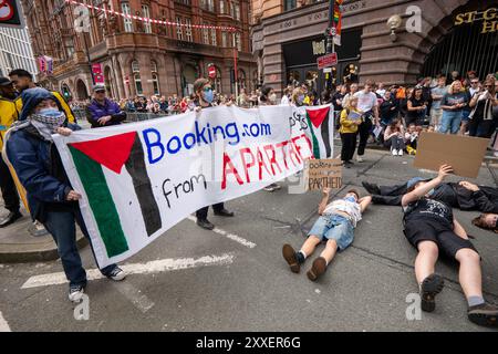 Manchester, UK. 24th Aug, 2024. Palestine Gaza war protesters laying in road ahead of Pride Parade. Palestinian protesters failed to prevent Pride Parade taking place after they blocked road on Peter Street by laying in road. They were objecting against Booking.com who also carry adverts for properties in Israel. The police moved in and cleared the protest allowing the protest to proceed. Some individuals in the parade where carrying Palestinian flags.Manchester Pride 2024 . This year's theme is 'Buzzin To Be Queer - A Hive of Progress' . The symbol of the Manchester Bee led the parade. Credit Stock Photo