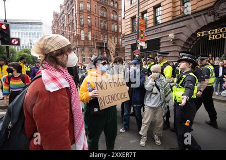 Manchester, UK. 24th Aug, 2024. Palestine war protesters are cleared by police on Peters Street ahead of Manchester Pride parade.Palestinian protesters failed to prevent Pride Parade taking place after they blocked road on Peter Street by laying in road. They were objecting against Booking.com who also carry adverts for properties in Israel. The police moved in and cleared the protest allowing the protest to proceed. Some individuals in the parade where carrying Palestinian flags.Manchester Pride 2024 . This year's theme is 'Buzzin To Be Queer - A Hive of Progress' . The symbol of the Manchest Stock Photo