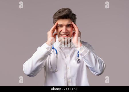 30s vecchio medico uomo in forma di cappotto medico bianco con mal di testa, studio ritratto. Tizio che mette le mani sulla testa, isolato su sfondo bianco. Concetto o Foto Stock