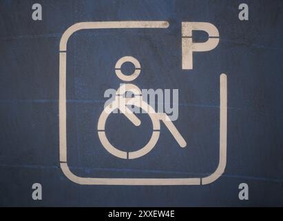 Dettaglio di un cartello dipinto in blu che indica uno spazio riservato ai disabili in un parcheggio pubblico. Logo di una sedia a rotelle Foto Stock