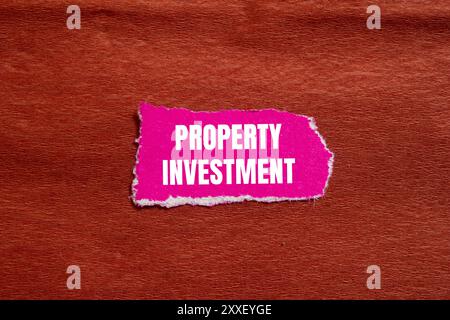 Messaggio di investimento immobiliare scritto su un pezzo di carta rosa strappato con sfondo marrone. Simbolo di investimento immobiliare concettuale. Copia spazio. Foto Stock