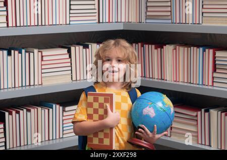 Ragazzo scolastico con globo mondiale e scacchi, infanzia. Torna a scuola. Bambino divertente della scuola elementare con il libro. Istruzione. I bambini studiano e. Foto Stock