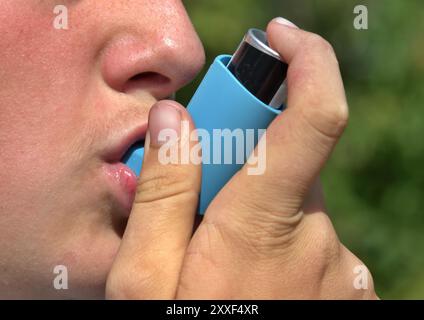 Primo piano di una persona che usa un inalatore blu all'aperto Foto Stock