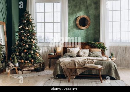 Grande letto matrimoniale con testiera in legno in una spaziosa camera da letto decorata per Natale. La luce del sole scorre attraverso grandi finestre, evidenziando il verde Foto Stock