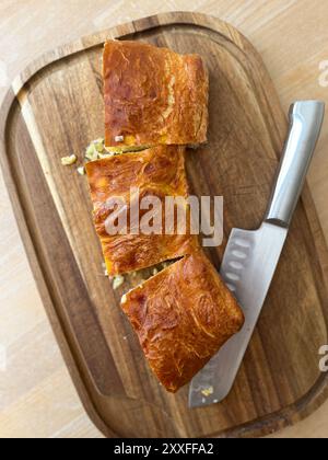 Vista dall'alto di tre pezzi di una torta di cavolo e un coltello moderno su un tagliere di legno su un tavolo alla luce del giorno Foto Stock