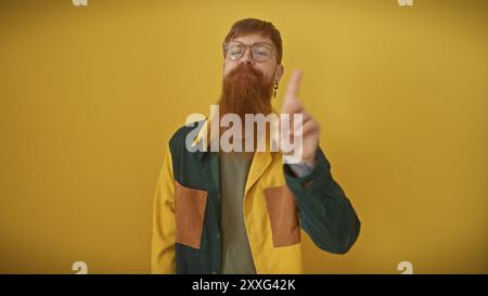 L'uomo con la barba rossa in occhiali puntati su uno sfondo giallo, sembra eccentrico e sicuro di sé. Foto Stock