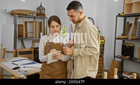 Uomo e donna, probabilmente partner, che lavorano insieme in un'officina di falegnameria, discutendo i piani di progettazione. Foto Stock