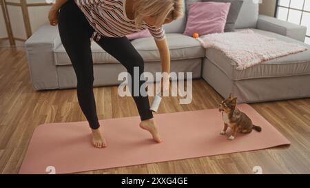 Giovane donna bionda con un cane chihuahua in salotto, che utilizza un rullo di lanugine e si trova su un tappetino rosa sopra i pavimenti di legno duro accanto Foto Stock