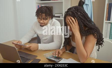 Una coppia stressata con una donna e un uomo che gestiscono le finanze in un ufficio domestico, con denaro, calcolatrice, laptop e documenti. Foto Stock
