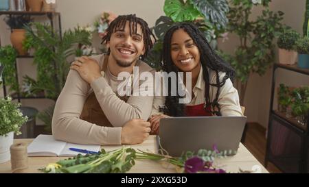 Una donna e un uomo sorridono mentre lavorano insieme in un negozio di fiori circondato da piante e composizioni floreali. Foto Stock